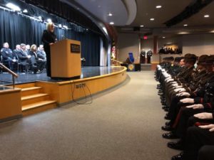 Jamie L. Dykes speaking from stage podium to auditorium of Academy graduates