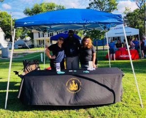 Man with 2 women staff posing behind National Night Out booth
