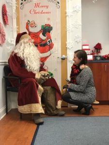 Seated Santa speaks to kneeling woman holding young child