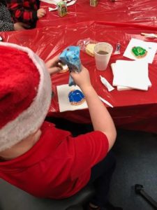 boy weating santa hat decorates festive cookie on table